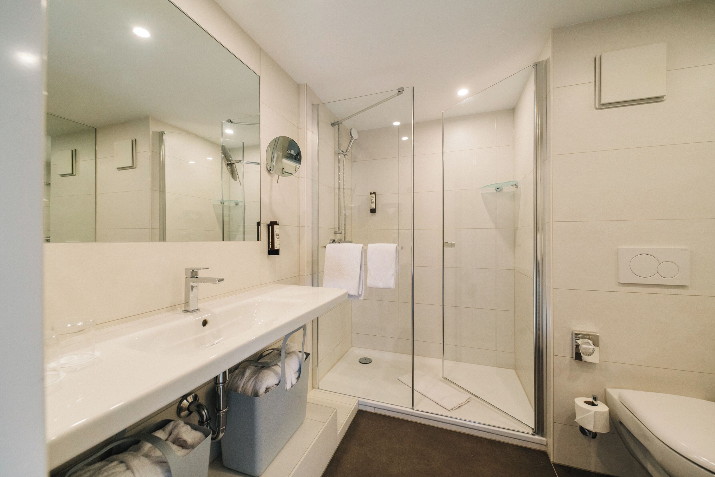 Une salle de bain moderne avec une douche à parois de verre, un grand miroir et un lavabo blanc.
