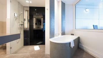 A modern bathroom with a glass shower enclosure, a freestanding bathtub, and a large window providing natural light.