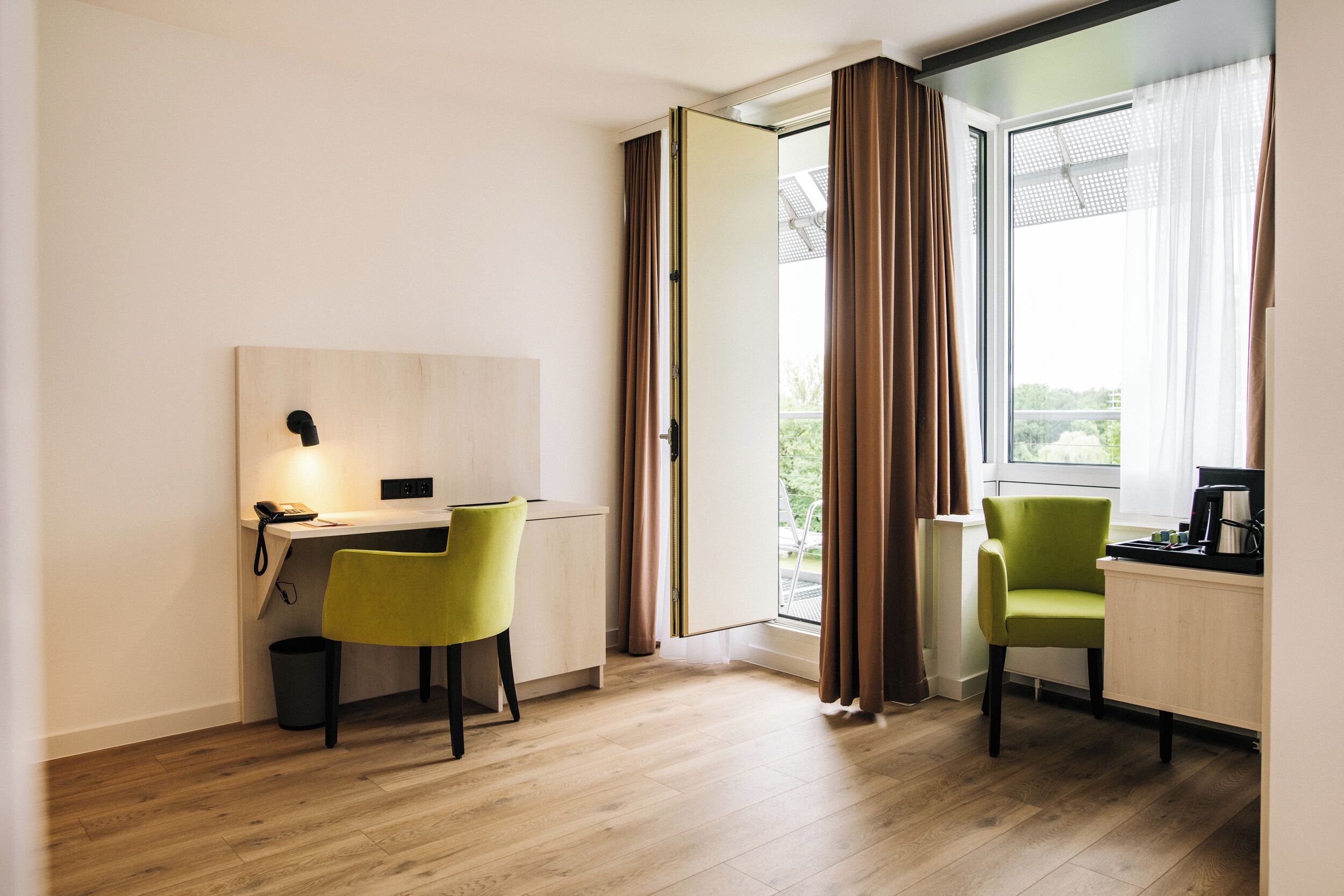 Une chambre d’hôtel moderne équipée d’un bureau, de deux chaises, d’un téléphone et d’une fenêtre avec des rideaux.