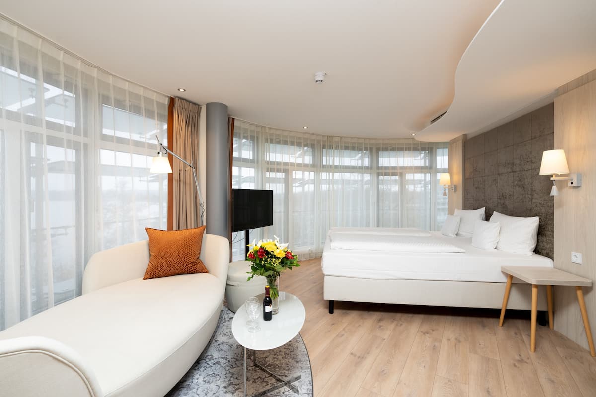 Una habitación de hotel moderna con sofá, cama, televisor y una mesita con un florero.