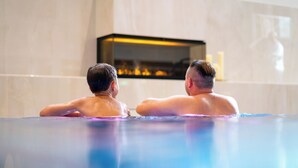 Twee personen in een bubbelbad met een modern interieur en een open haard op de achtergrond.