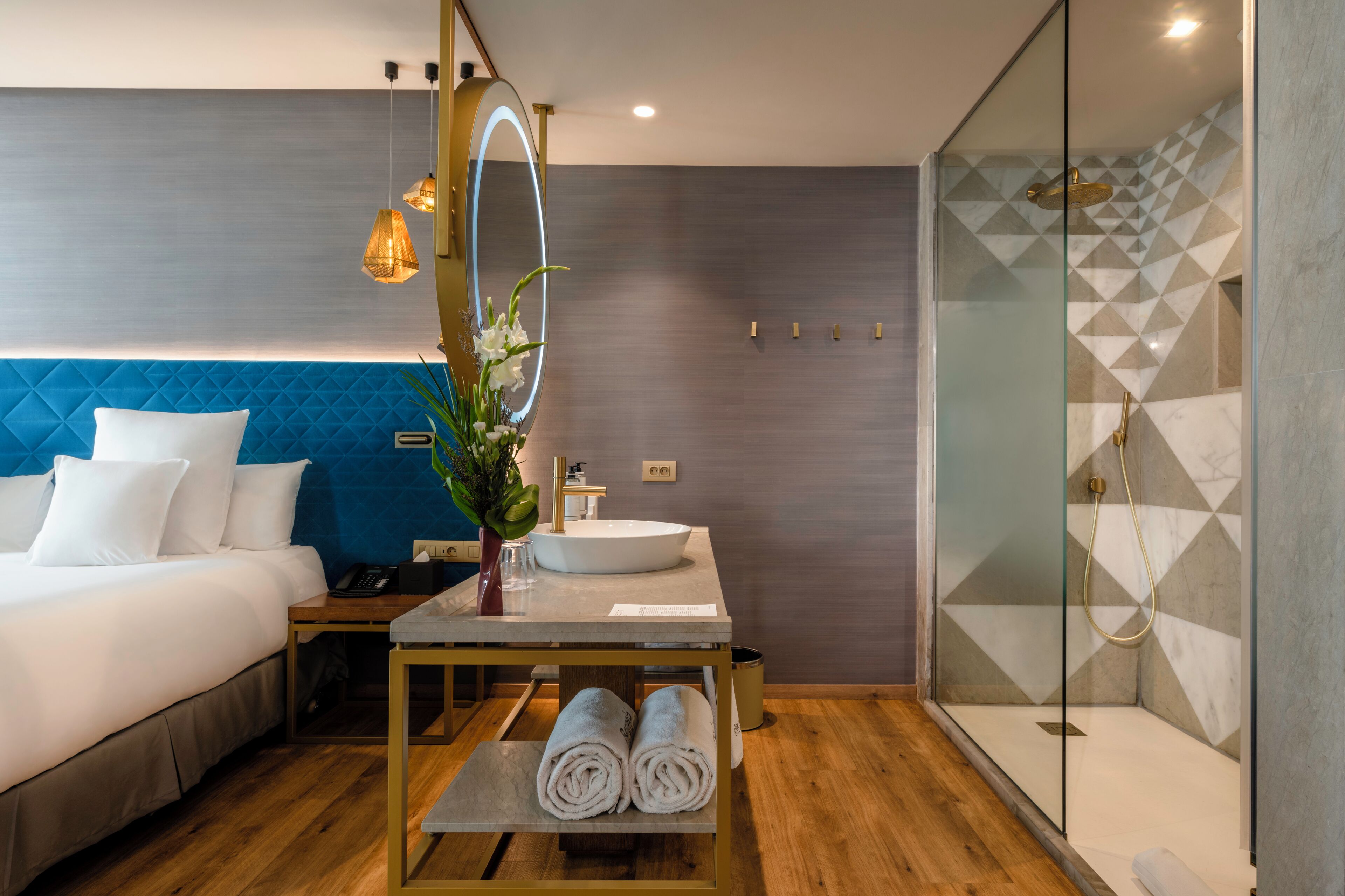 Ein modernes Hotelzimmer mit Bett, Nachttisch, Spiegel, Waschbecken und Dusche.
