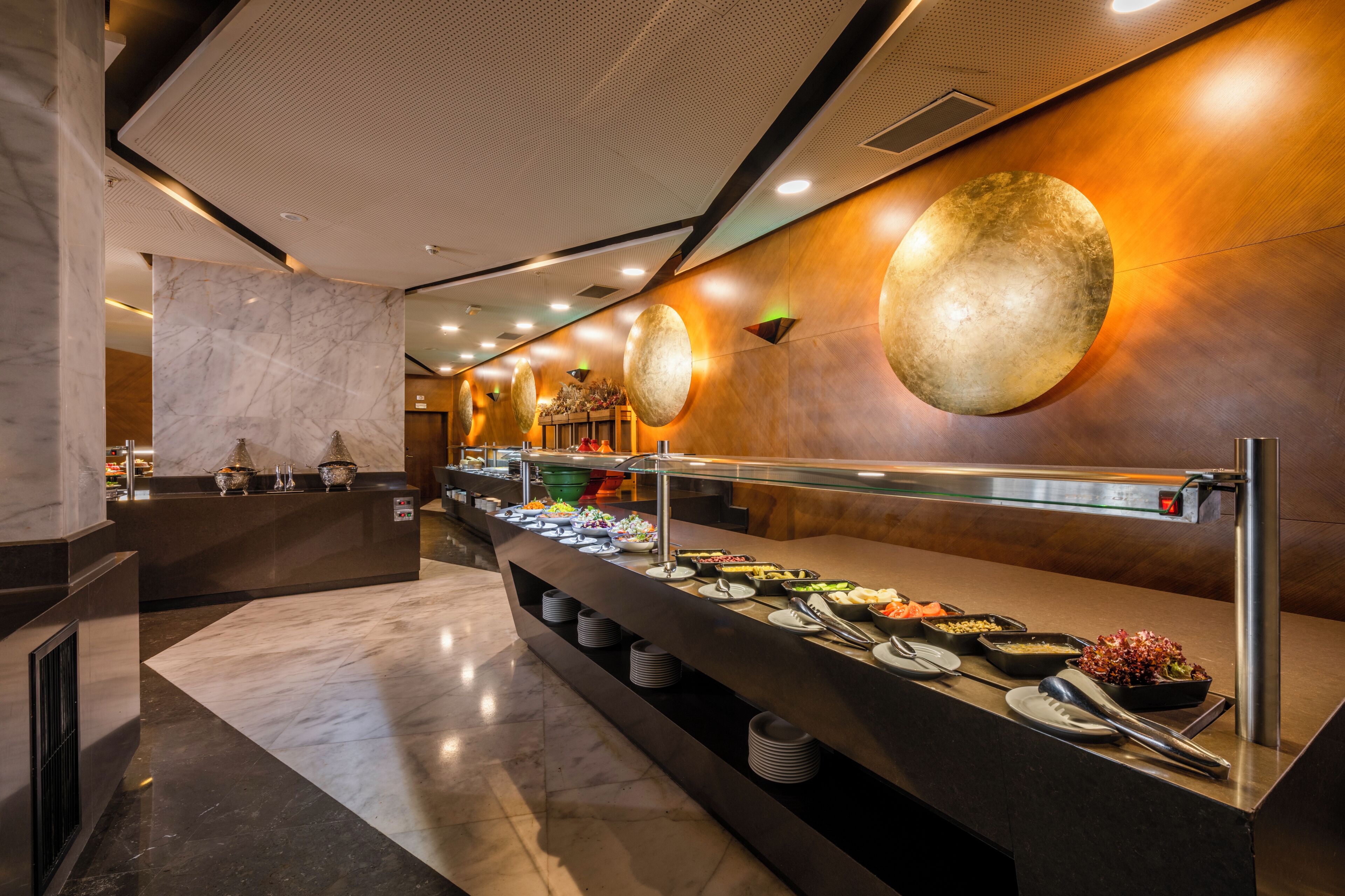 Zona de bufé con mostrador de mármol, diferentes platos de comida y una pared moderna con detalles decorativos circulares.