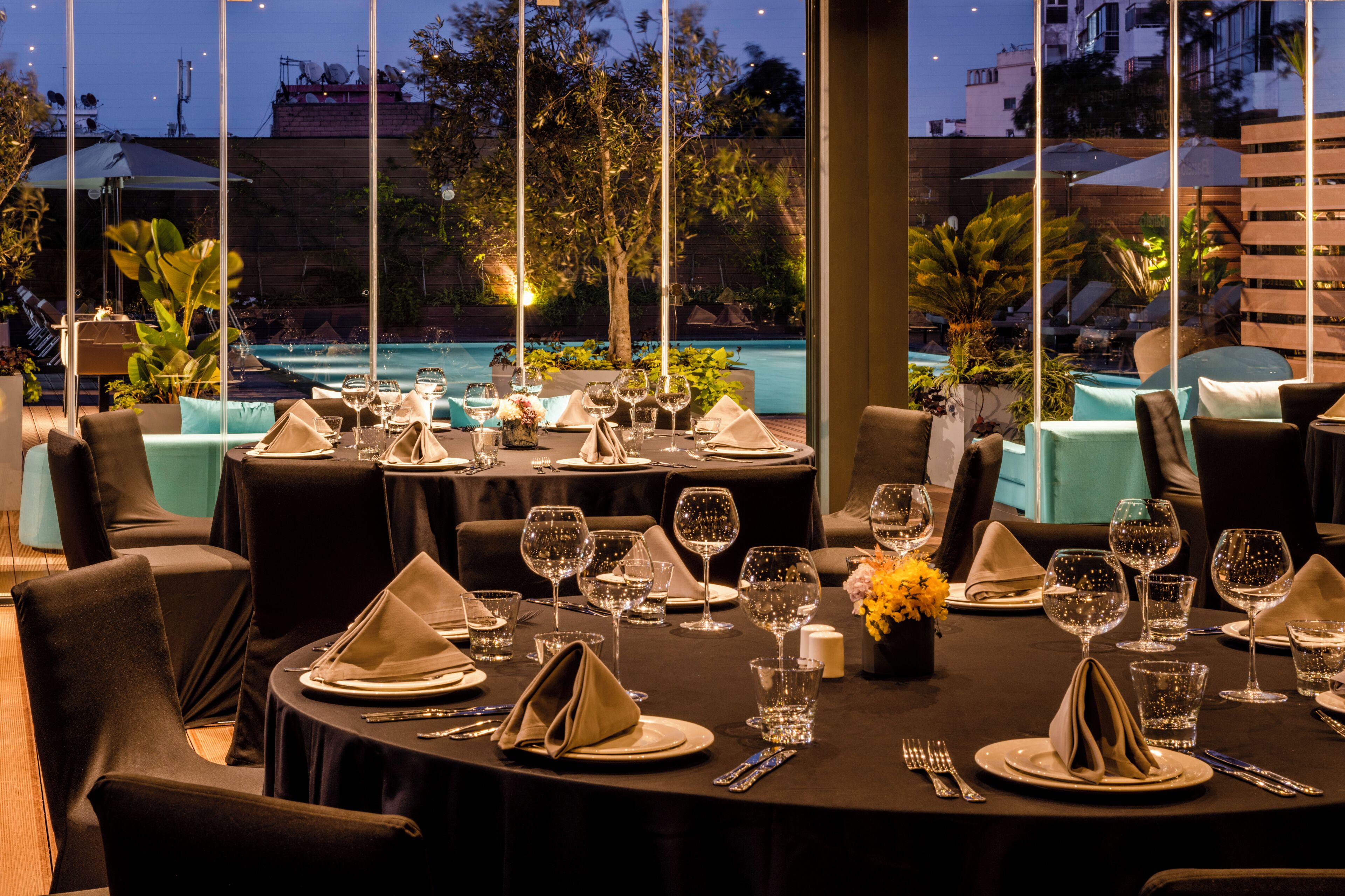 A dining area with tables set for a meal, a pool in the background, and outdoor seating.