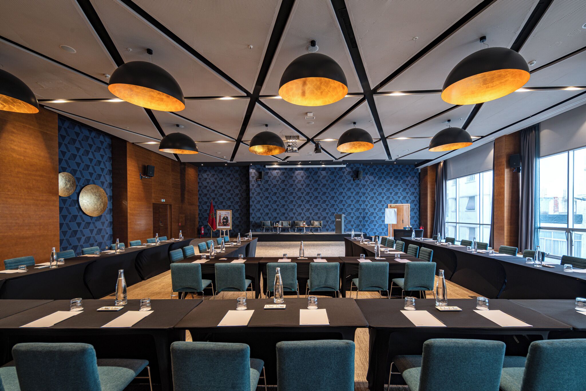 Un salón de conferencias con una mesa larga, sillas azules e iluminación colgante.