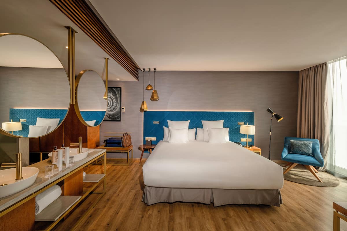 A hotel room with a large bed, a vanity with a mirror, a desk, and a chair.