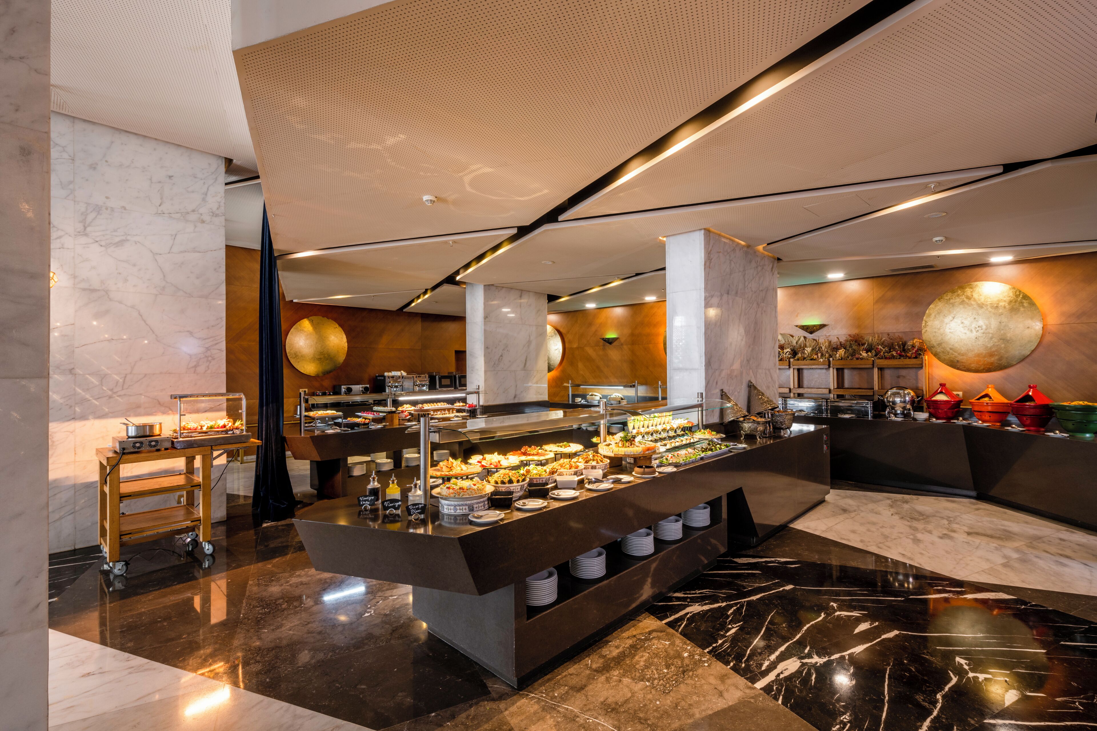 A buffet setup with a marble floor, a central serving counter, and a variety of food items.