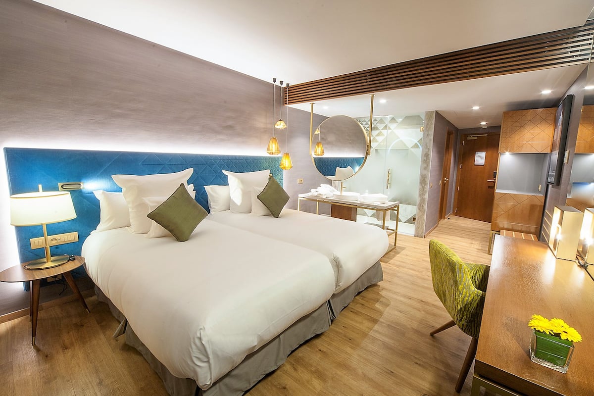 A hotel room with a large bed, bedside tables, a desk, a chair, a mirror, and a small table with flowers.