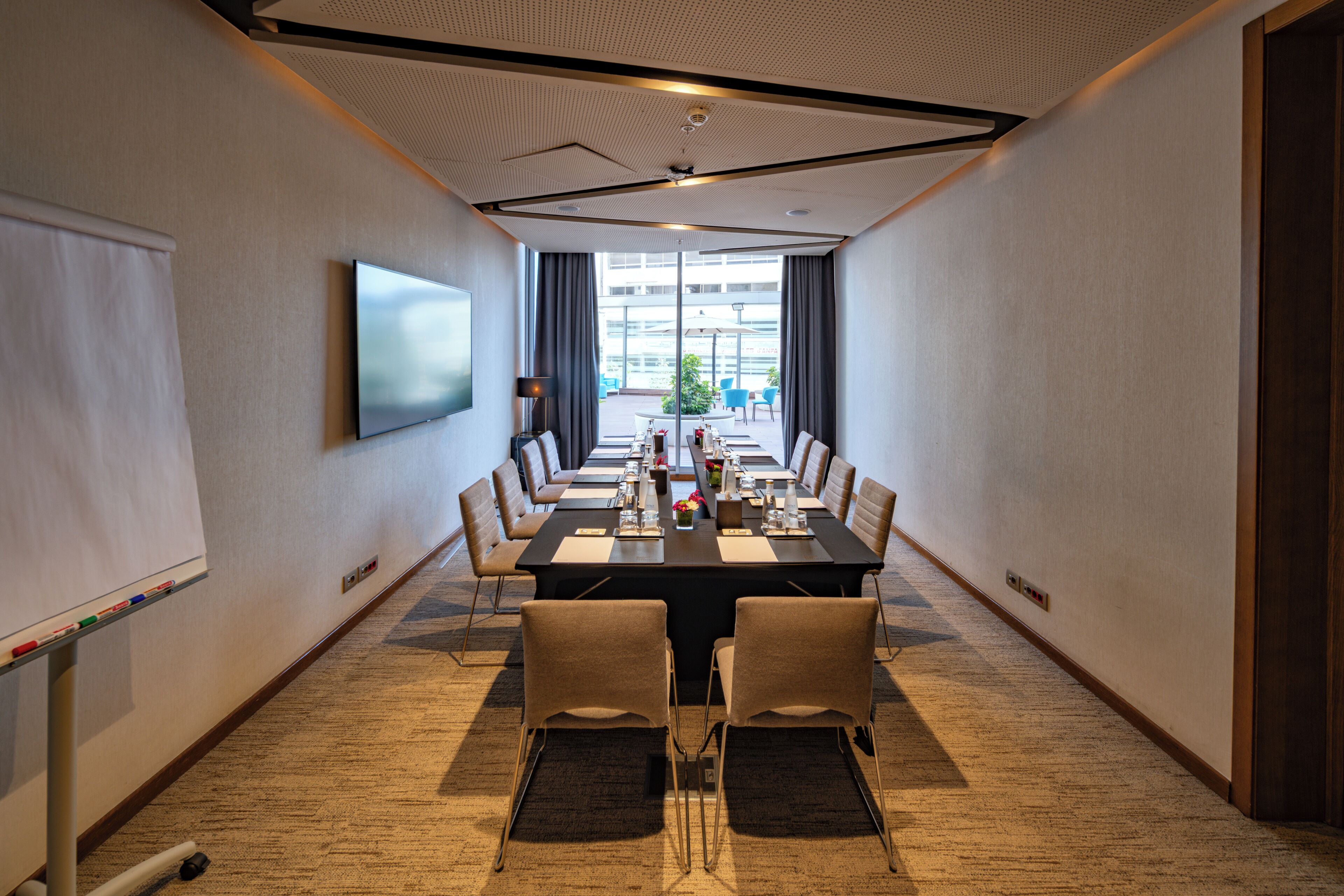 A conference room with a long table, chairs, a whiteboard, and a TV screen.