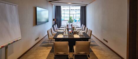 A conference room with a long table, chairs, a whiteboard, and a TV screen.