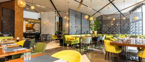 Un restaurante moderno con techos altos, patrones geométricos en las paredes y asientos en tonos amarillo y verde.