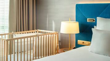 Une chambre d’hôtel avec un berceau, une lampe de chevet, un lit avec une literie blanche et une tête de lit bleue.