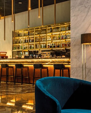 Eine Bar mit einer Säule aus Marmor, Barhocker und einem blauen, gepolsterten Sessel.