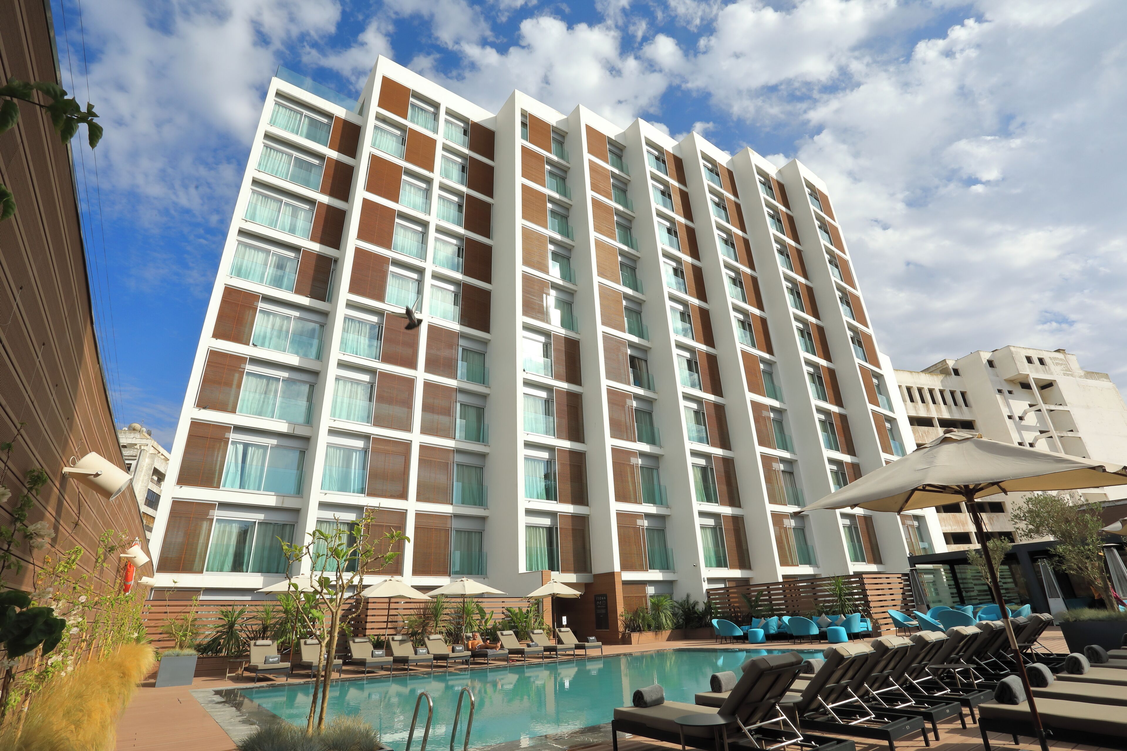 A hotel with a pool area, lounge chairs, and a large building with multiple floors and balconies.