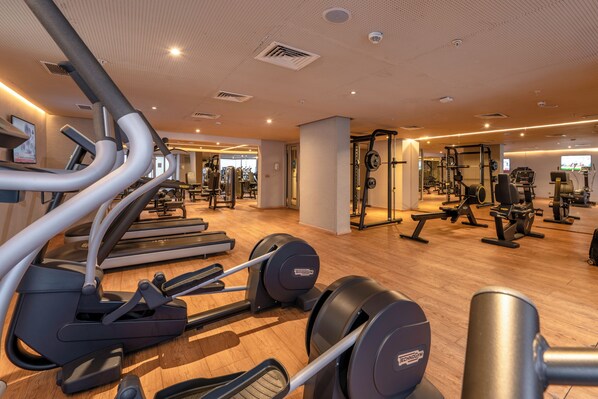 Un gimnasio con cintas de correr, elípticas y equipo de levantamiento de pesas.