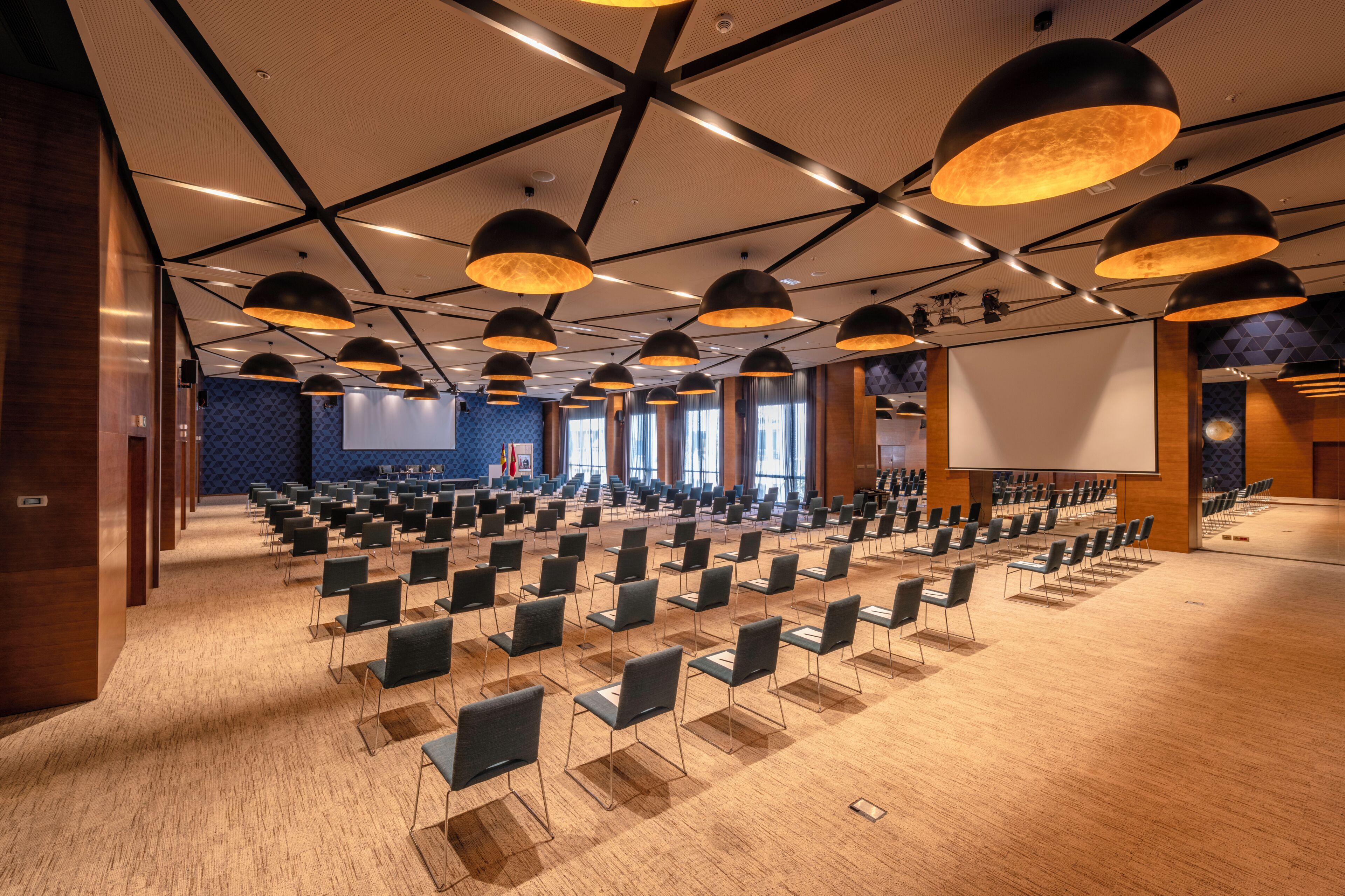 A conference room with rows of chairs, a large screen, and pendant lighting.