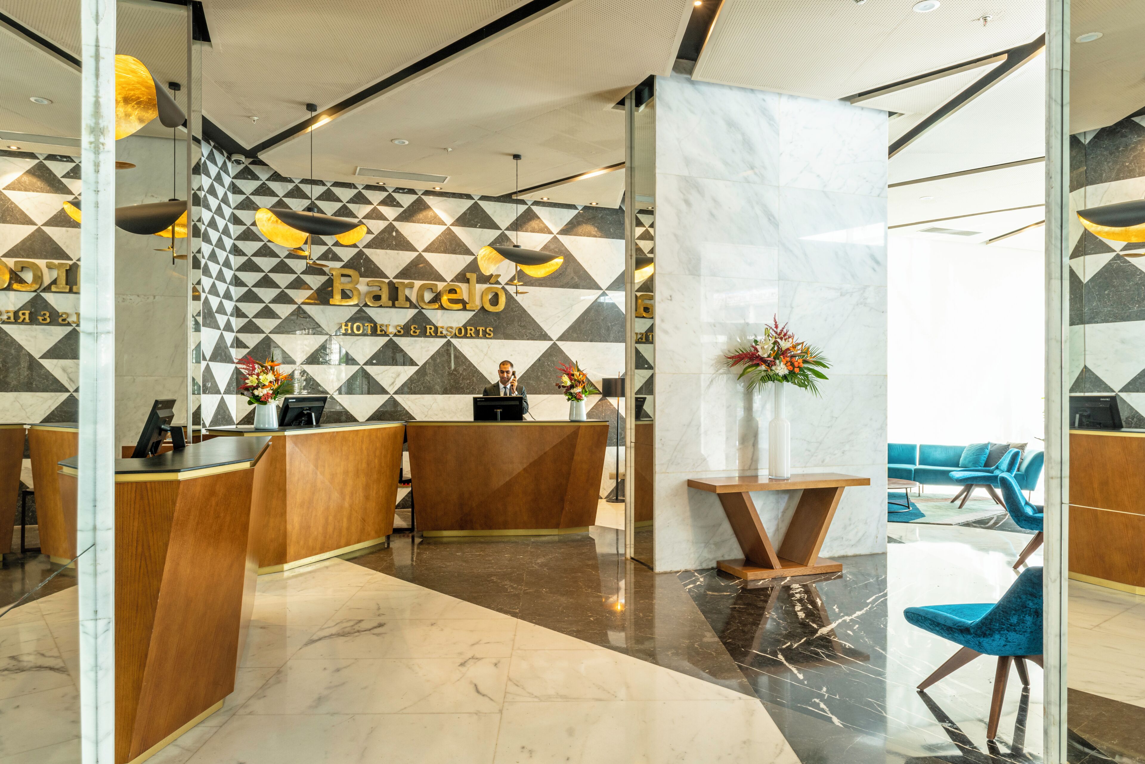 Een hotel receptie met een wand met geometrisch patroon, een marmeren balie en moderne zitplaatsen.