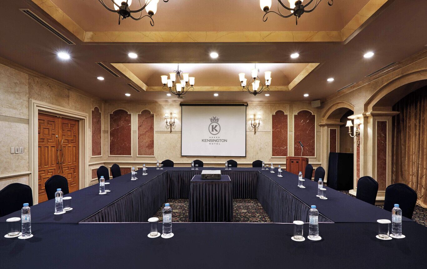 A conference room with a long table, water bottles, and a screen displaying the hotel name.