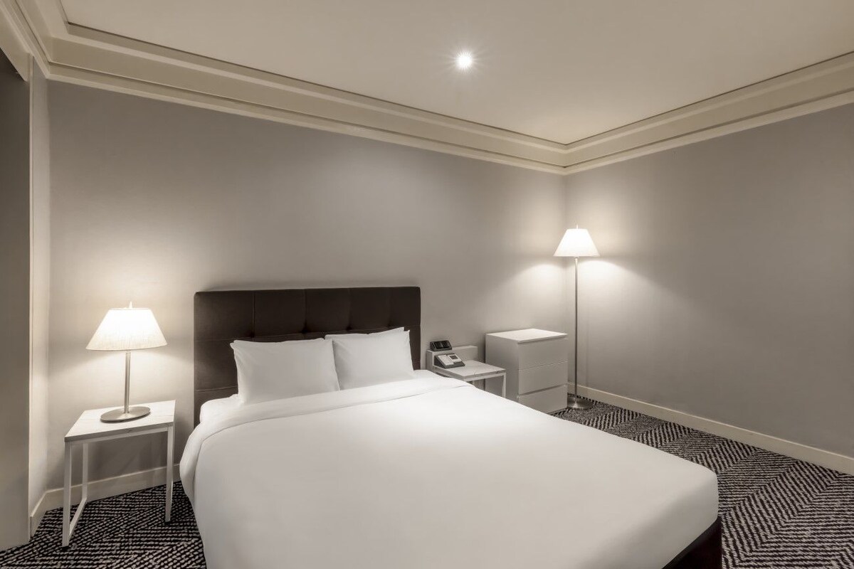 A hotel room with a large bed, two bedside tables, a nightstand, and a lamp.