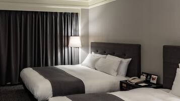 A hotel room with two beds, a nightstand with a telephone, and a lamp.