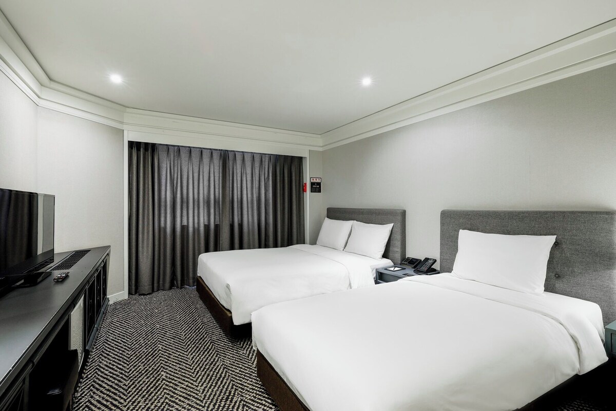 Une chambre d’hôtel avec deux lits, un bureau équipé d’un ordinateur, un téléphone et une télévision.