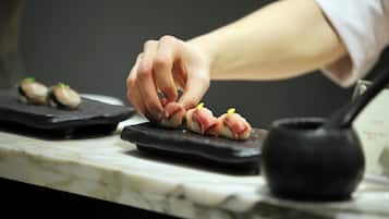 La main d’un chef déposant un morceau de sushi sur une assiette en ardoise noire.