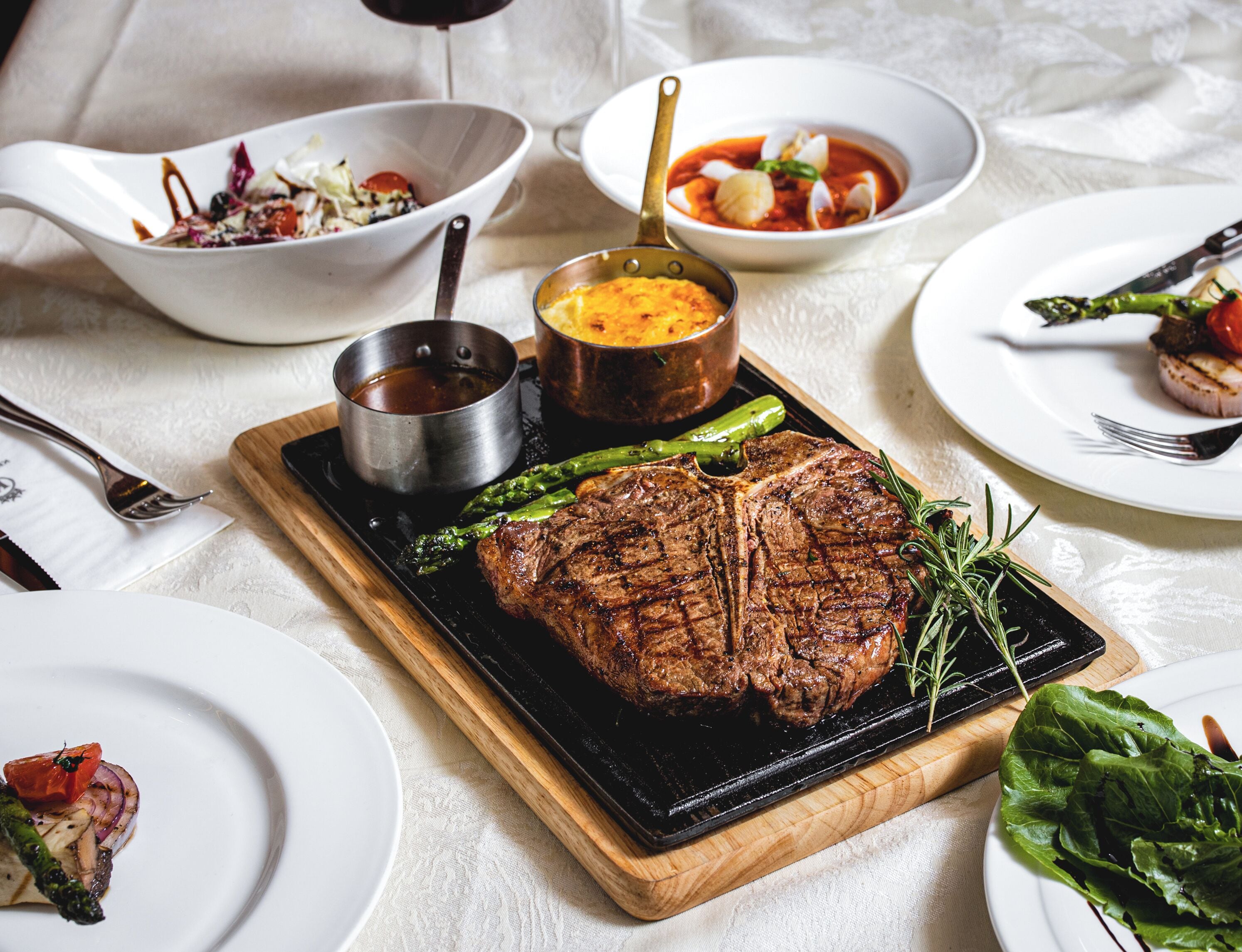 Ein festlich gedeckter Tisch mit einem gegrillten Steak, Spargel und verschiedenen Beilagen.