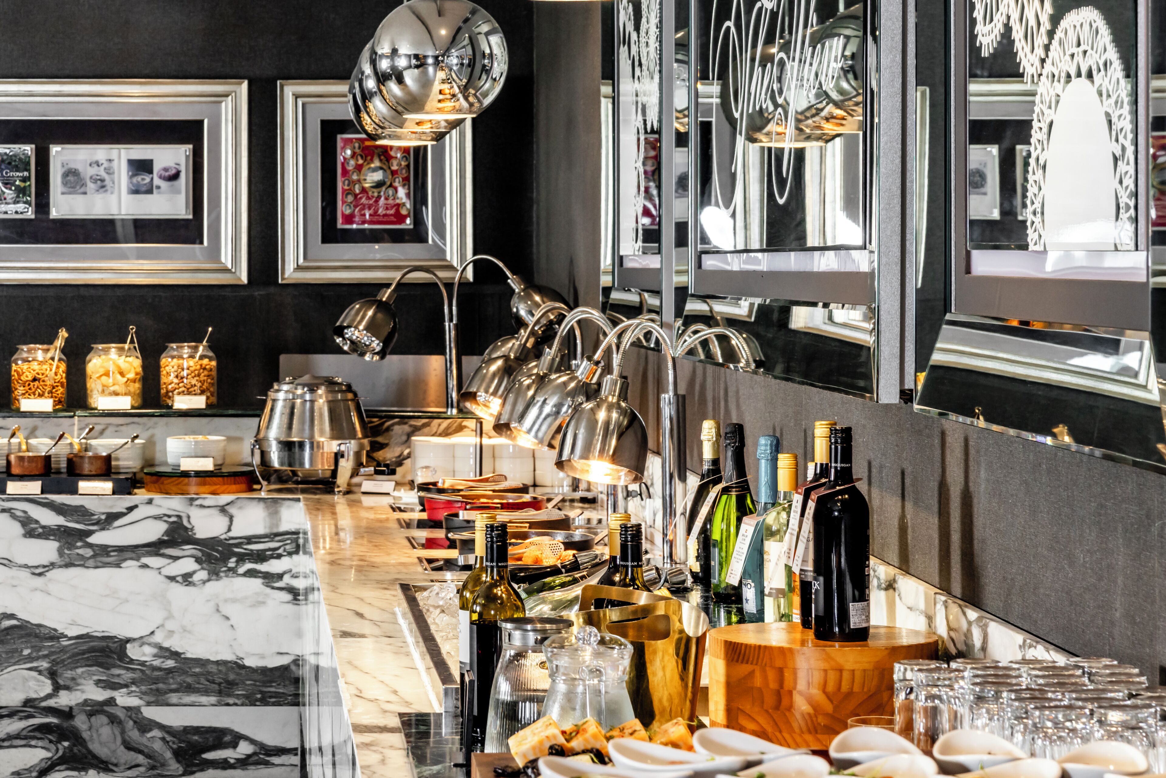 A bar area with a marble countertop, various bottles, glasses, and a modern light fixture.