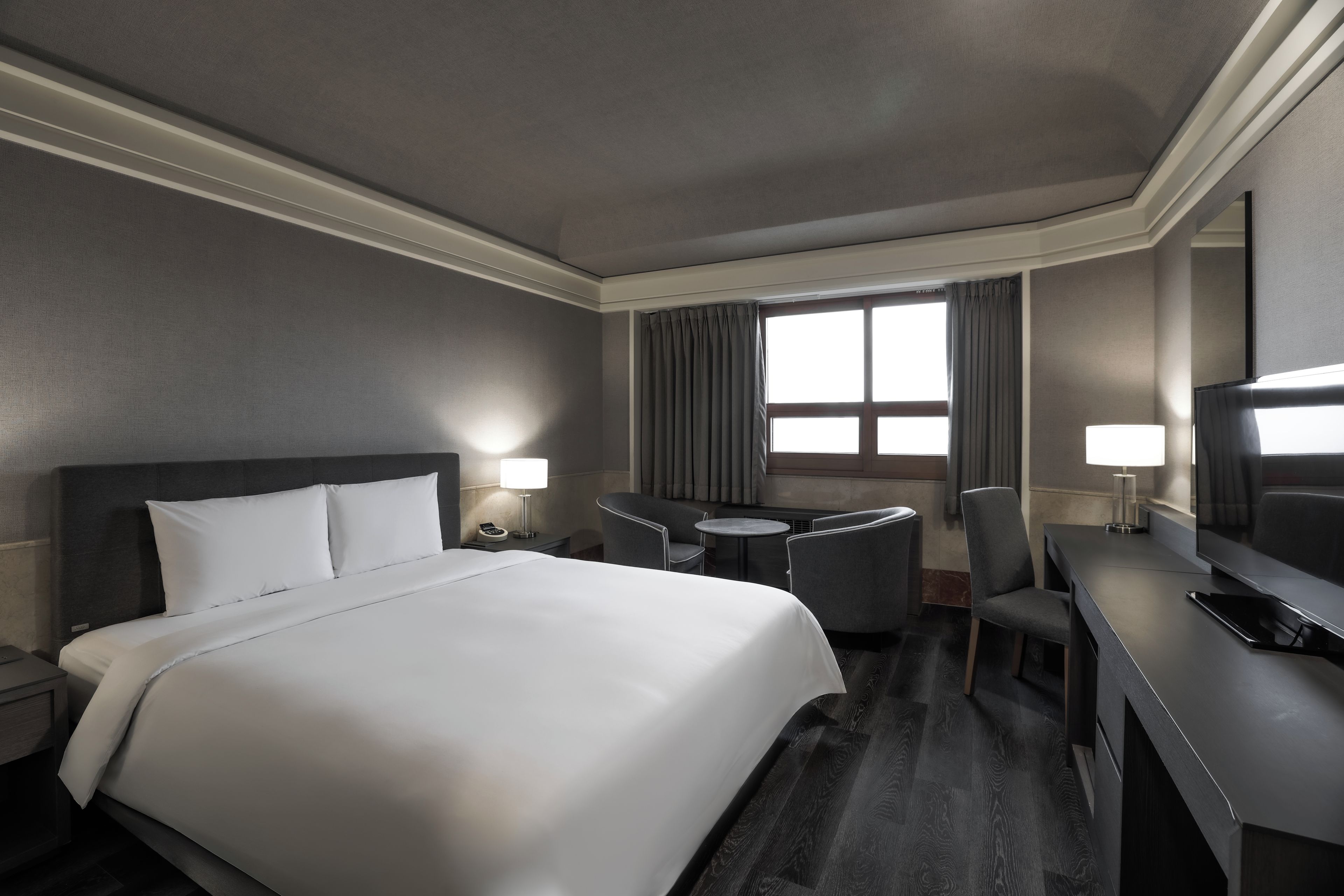 A hotel room with a large bed, a desk, a chair, a television, and a window with curtains.