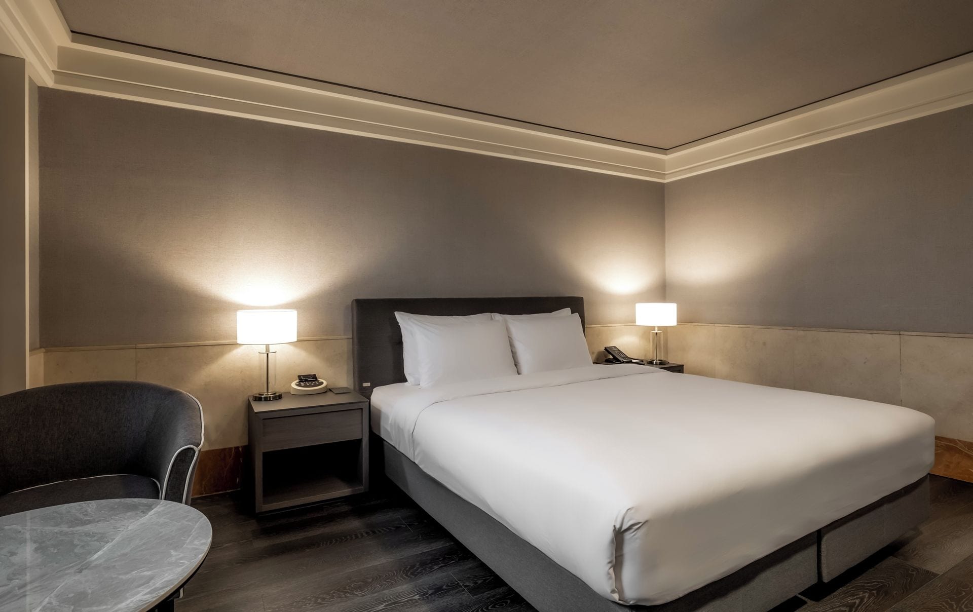 A hotel room with a large bed, two bedside tables with lamps, a chair, and a small table.
