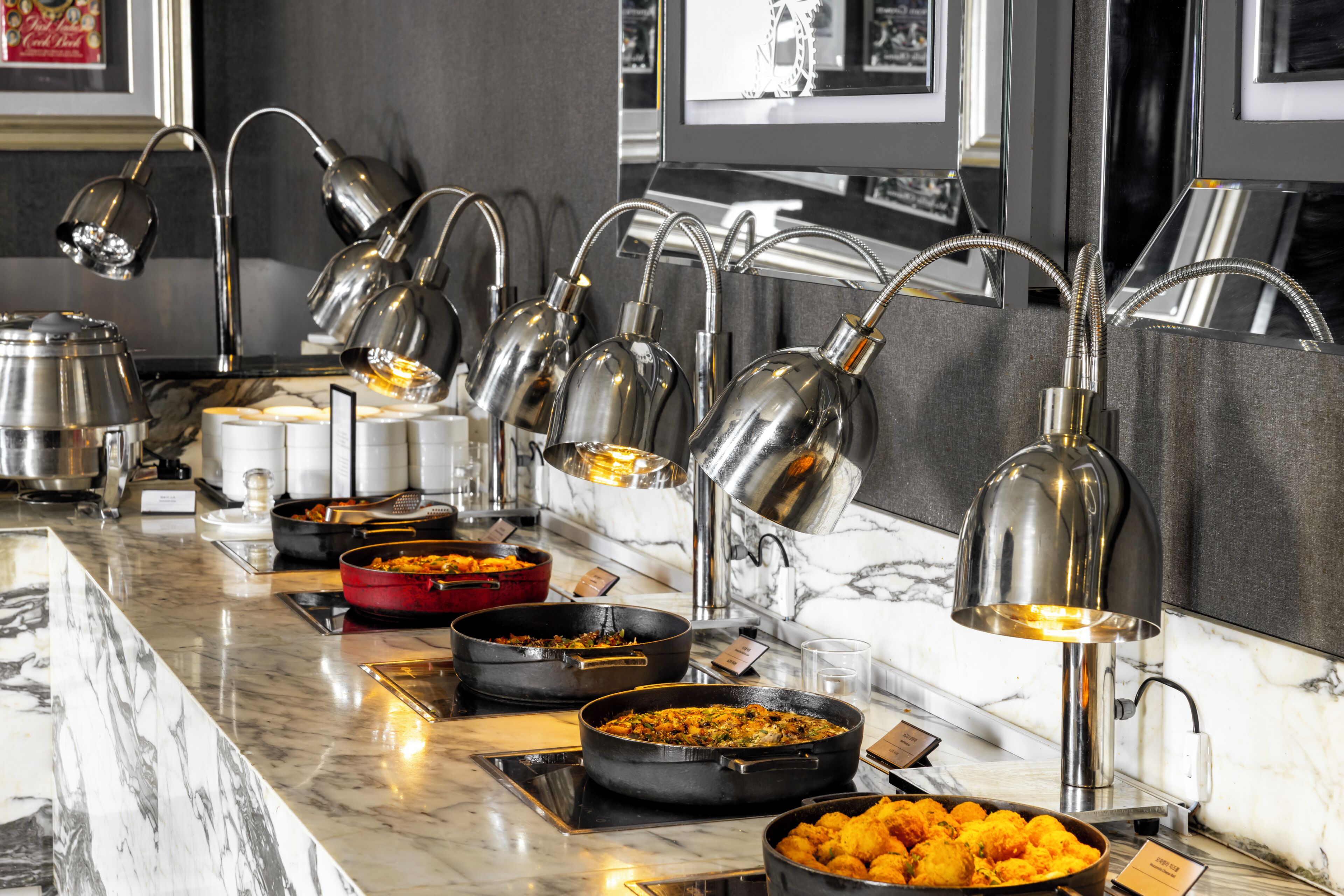 A buffet setup with multiple serving stations, each equipped with a metal bowl and a lamp.