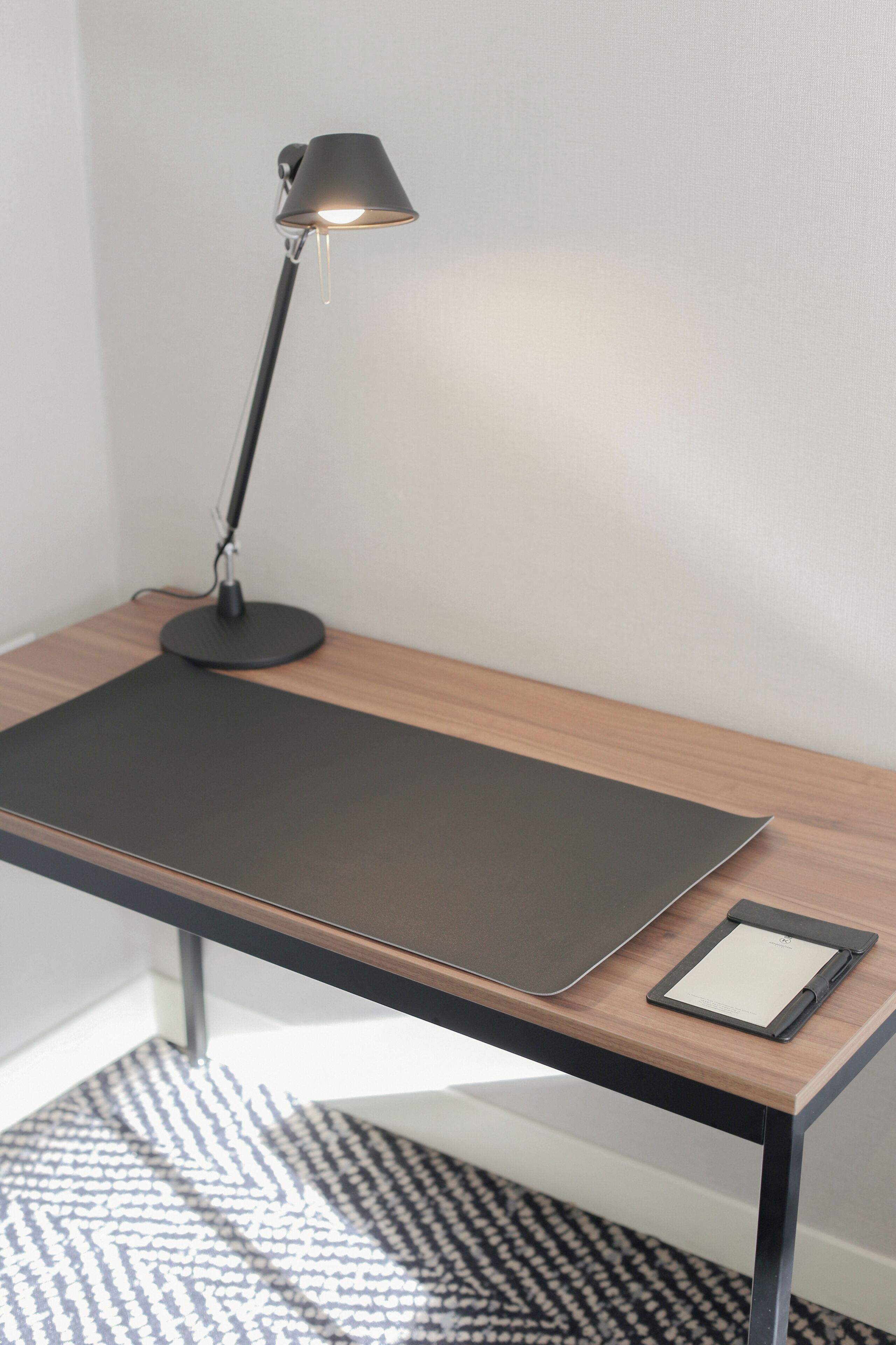 A desk with a black desk pad, a black lamp, and a tablet.