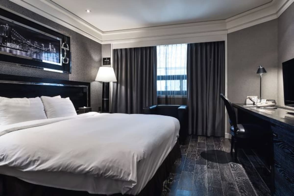 A hotel room with a large bed, a desk, a chair, a TV, and a window with curtains.