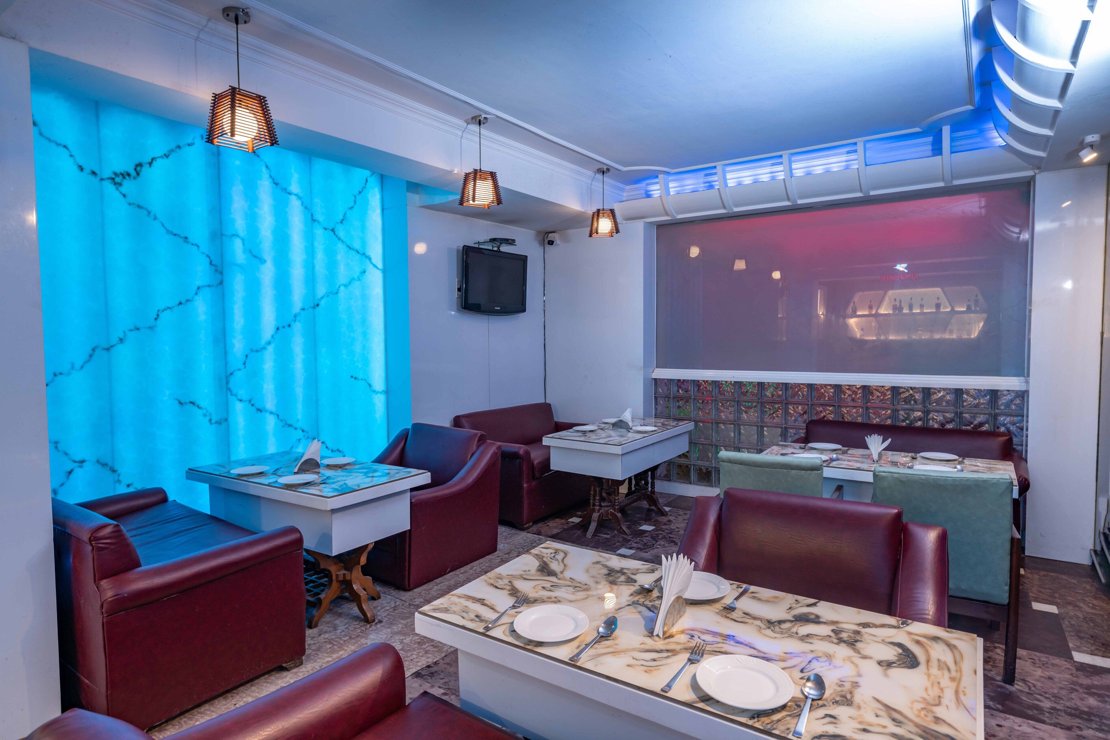 A restaurant with marble-topped tables, red leather booths, and blue lighting.