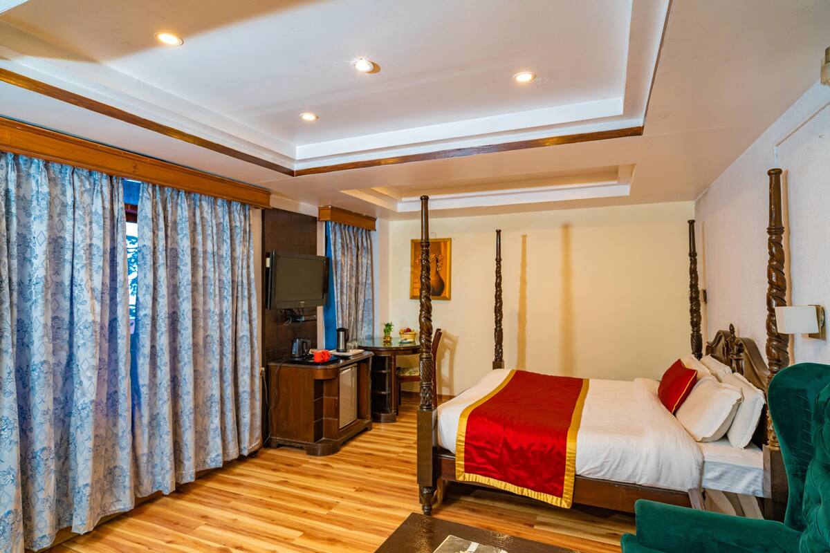 A hotel room with a four-poster bed, wooden flooring, a desk with a chair, and a television.