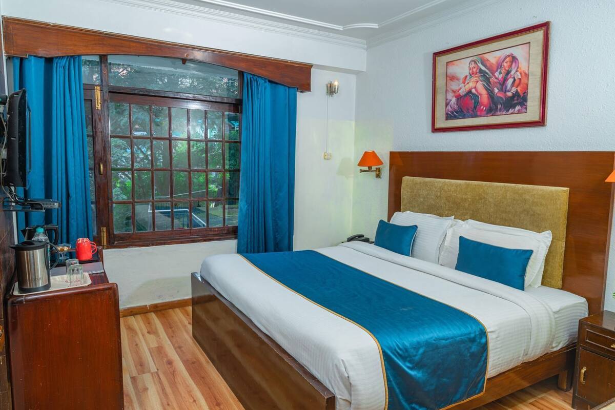 A hotel room with a large bed, a wooden nightstand, a coffee maker, a telephone, and a window with curtains.