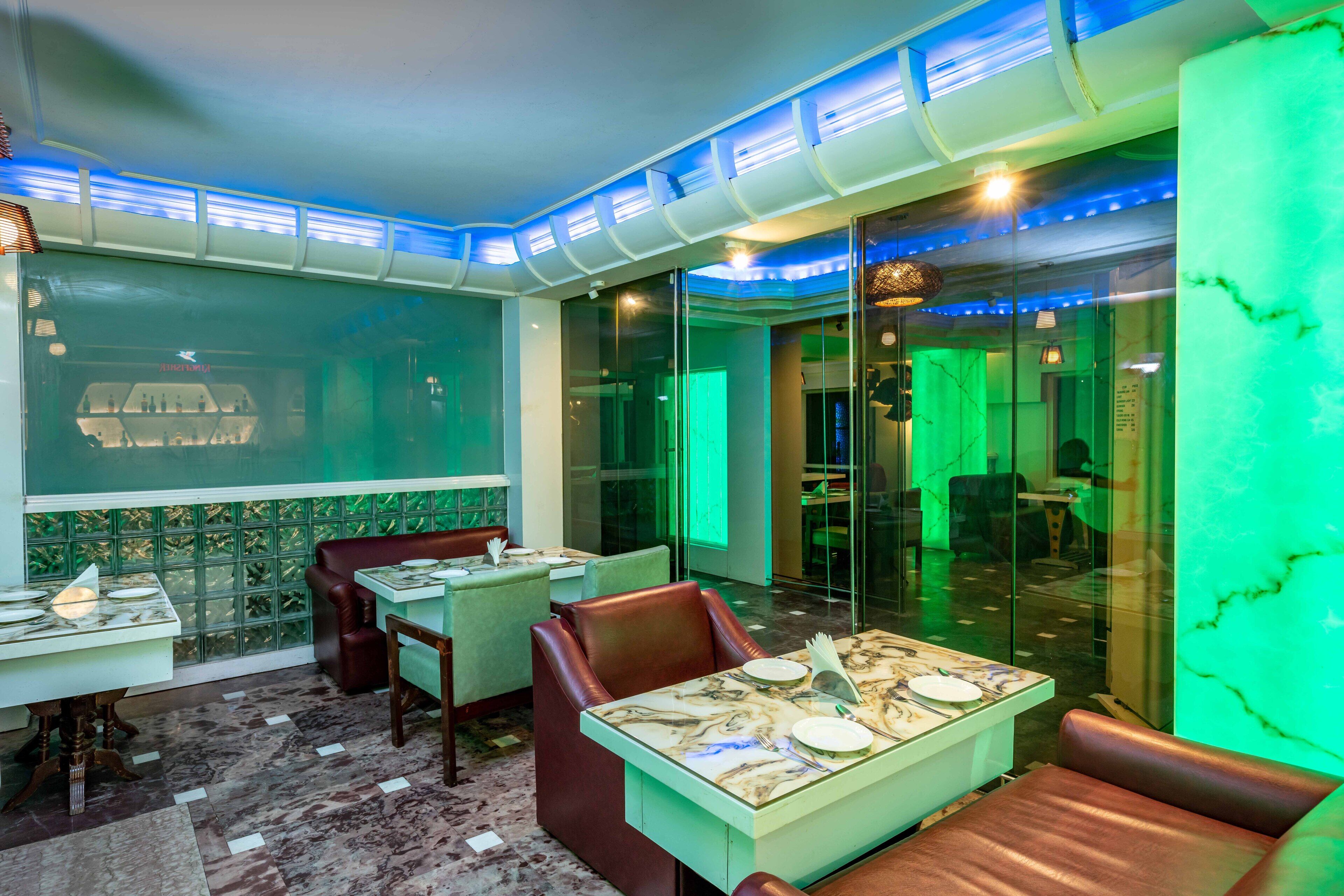 A restaurant with tables set for dining, glass partitions, and a green-lit ceiling.
