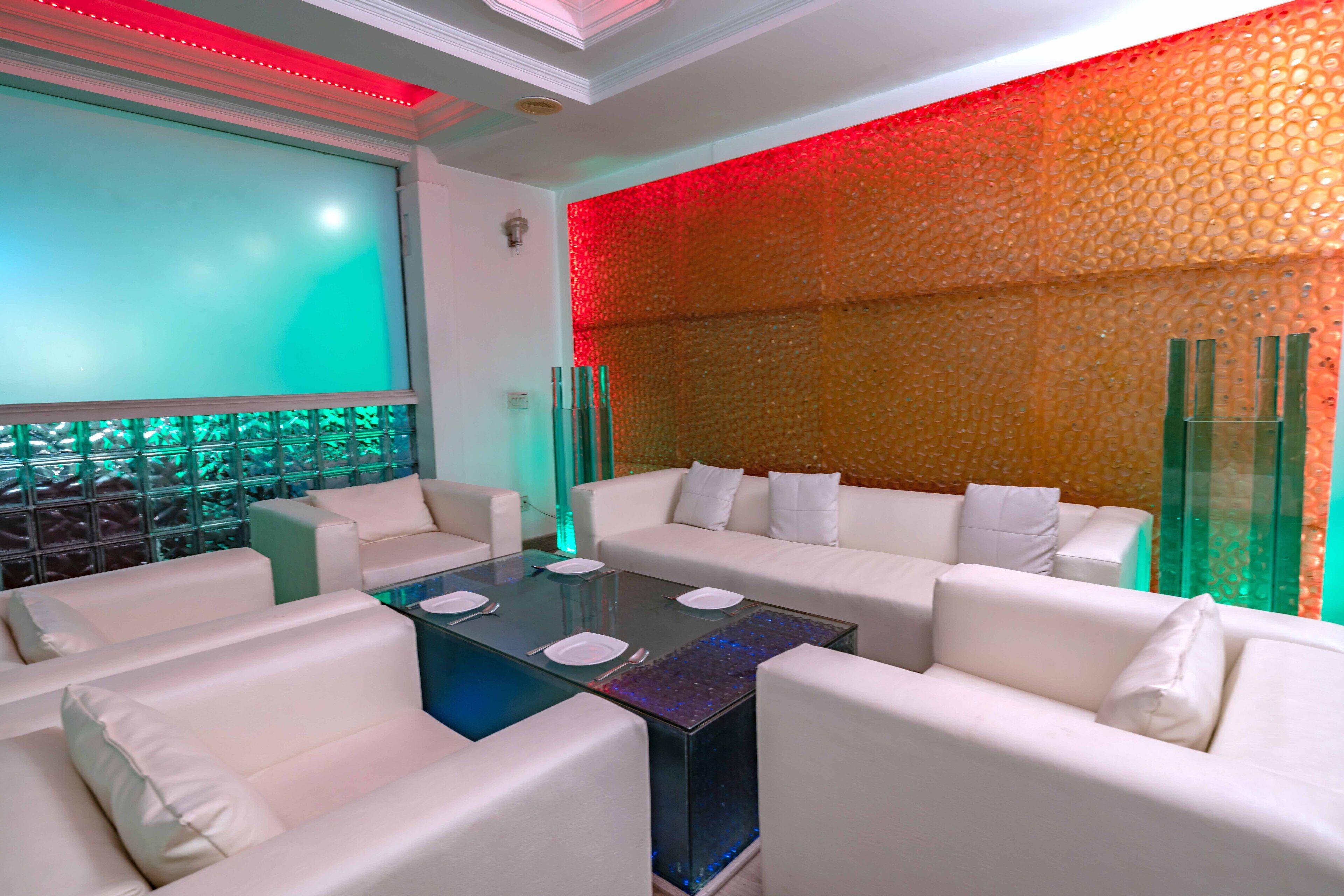 A modern lounge area with white sofas, a glass coffee table, and a decorative wall with a textured pattern.