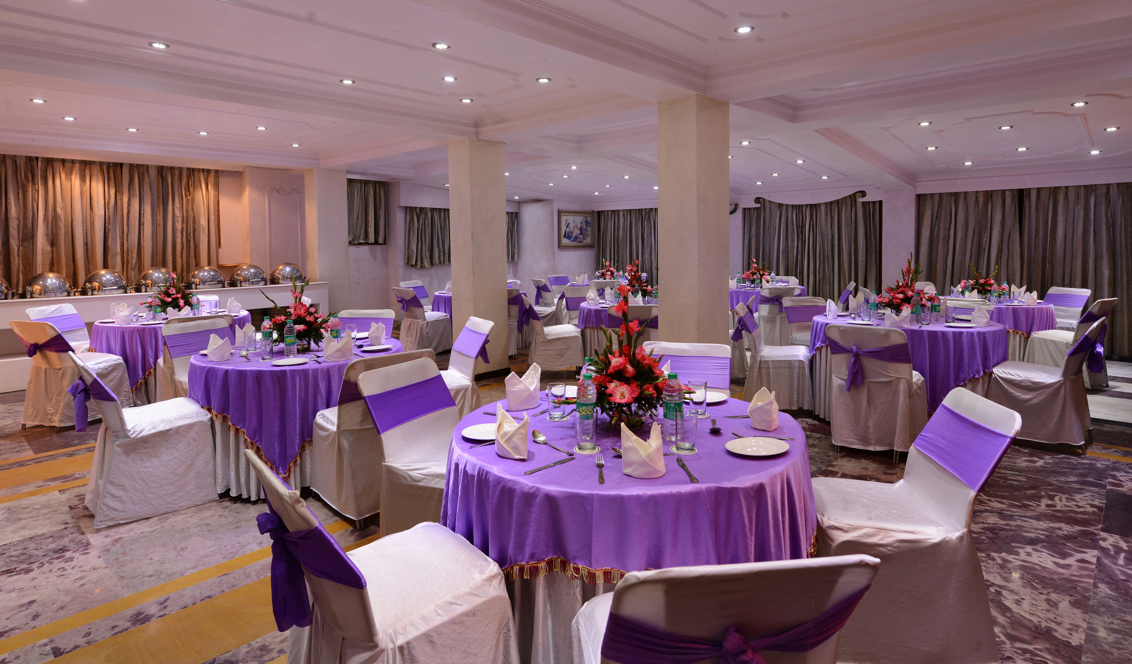 Ein Bankettsaal mit runden Tischen, bedeckt mit violetten Tischdecken, weißen Stühlen mit violetten Bändern und floralen Mittelpunkten.