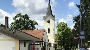 En gatubild med en kyrka som har ett högt torn och en klocka, en busshållplats och en skylt med ett telefonnummer.