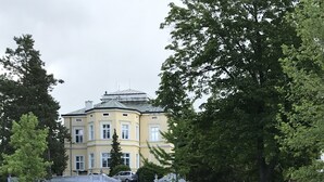 A large, multi-story building with a yellow facade and white trim, surrounded by a well-maintained lawn and trees.