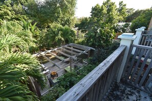 A wooden deck with a metal railing, surrounded by lush greenery and trees. - The Sugar Apple Lodging (Dunmore Town)