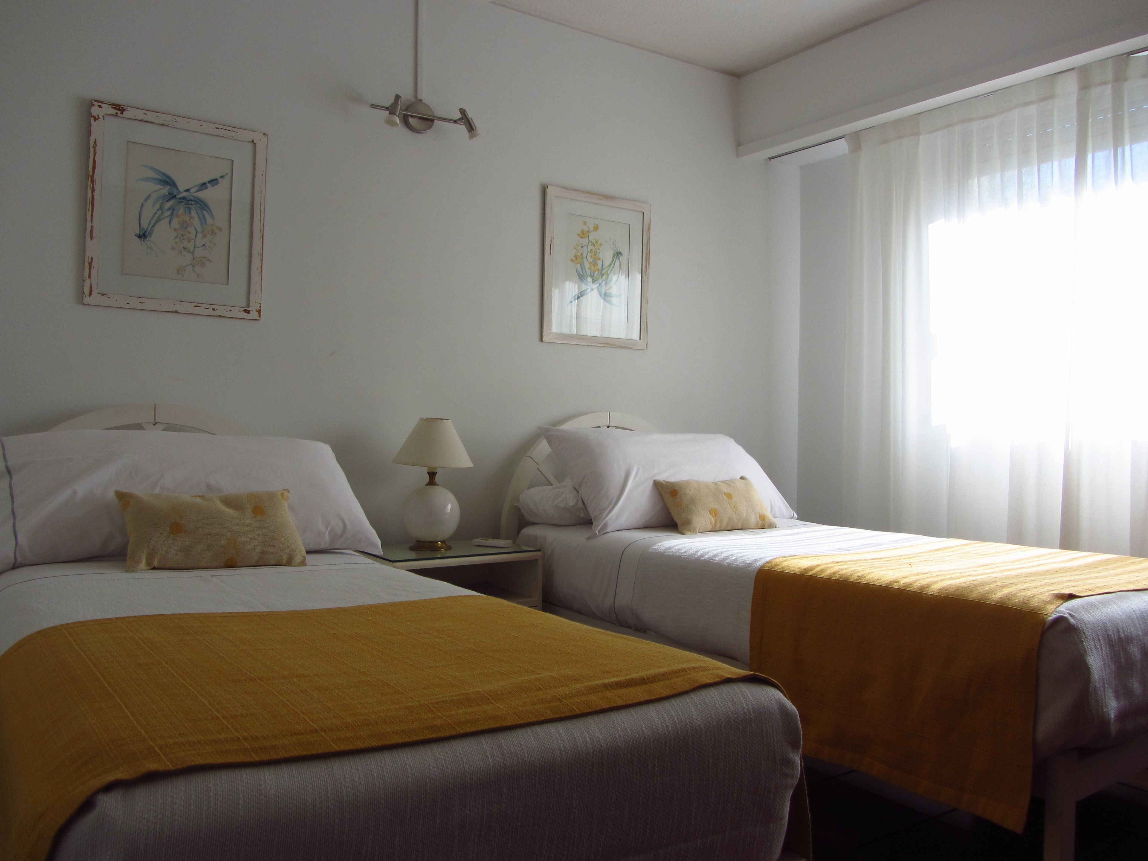 A hotel room with two beds, a nightstand with a lamp, and two framed pictures on the wall.