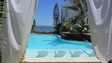 Una piscina al aire libre, sombrillas, sillones reclinables de piscina