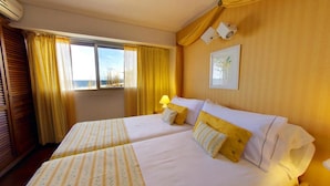Habitación de hotel con dos camas, una ventana con cortinas, una lámpara y un aplique de pared.