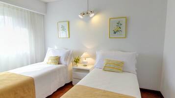 Una habitación de hotel con dos camas individuales, una mesita de noche con lámpara y dos impresiones botánicas enmarcadas en la pared.