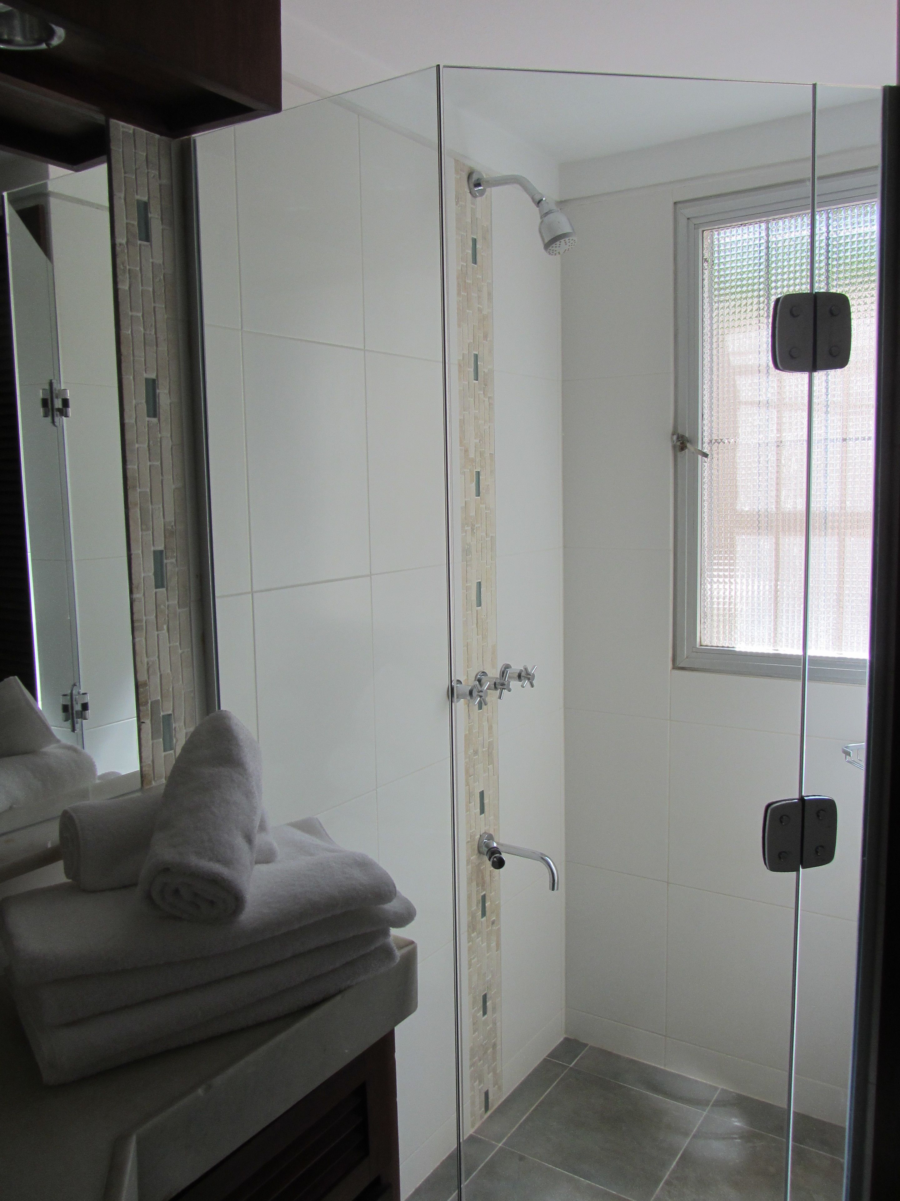 Een moderne badkamer met een douchecabine van glas, een witte betegelde wand en een raam met zonwering.