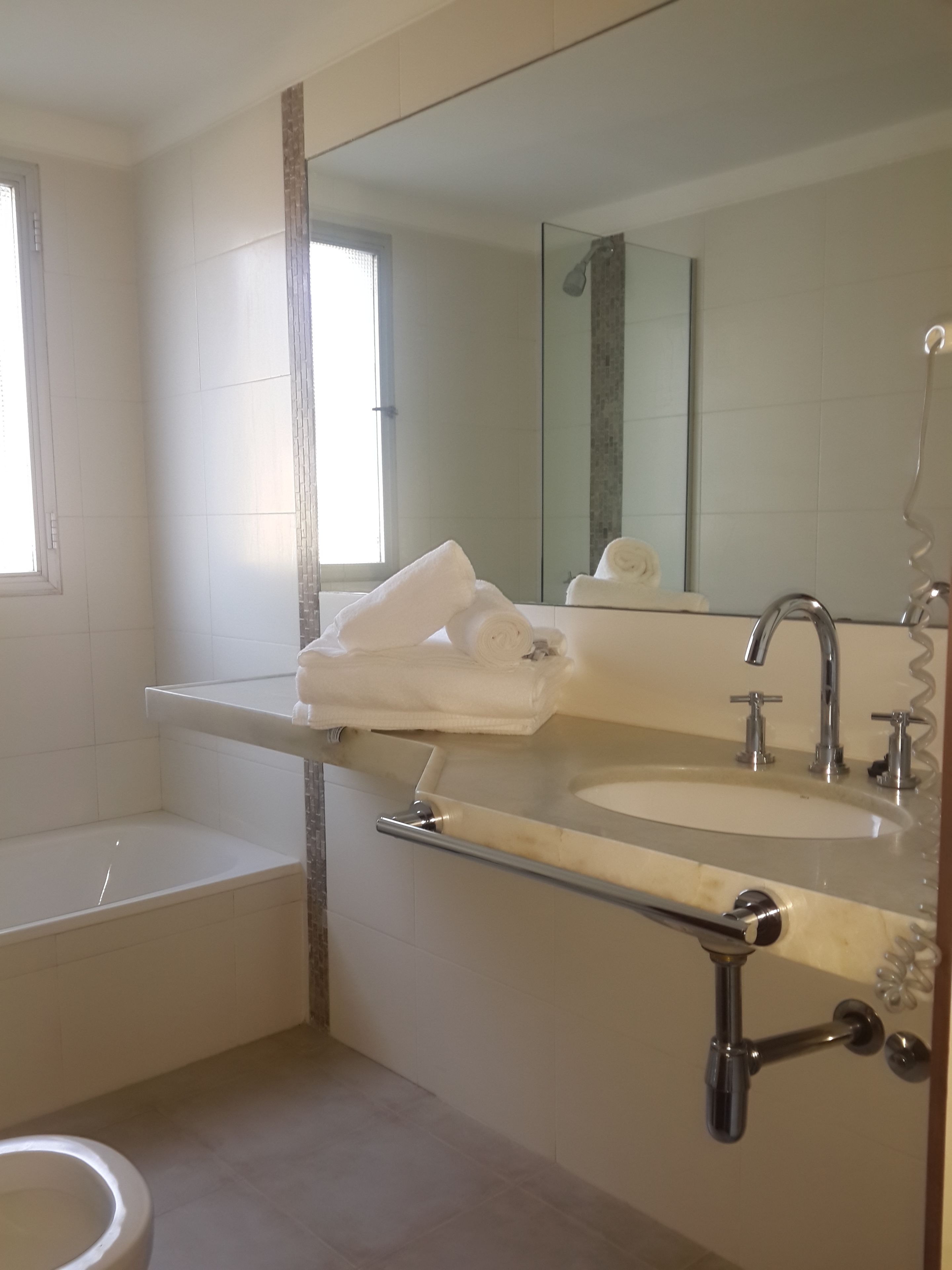 Un baño con bañera, lavamanos con espejo y toallero.