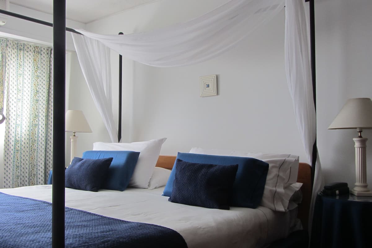 Ein Hotelzimmer mit Bett, zwei Nachttischlampen, einem Nachttisch und einem Fenster mit Vorhängen.