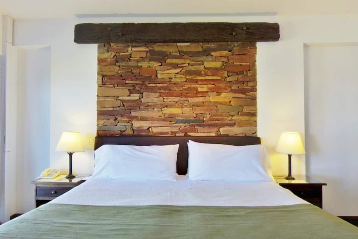 Ein Hotelzimmer mit einem Steinkopf am Kopfteil, zwei Nachttischlampen, einem Bett mit weißen Bettwäsche und einer grünen Tagesdecke.